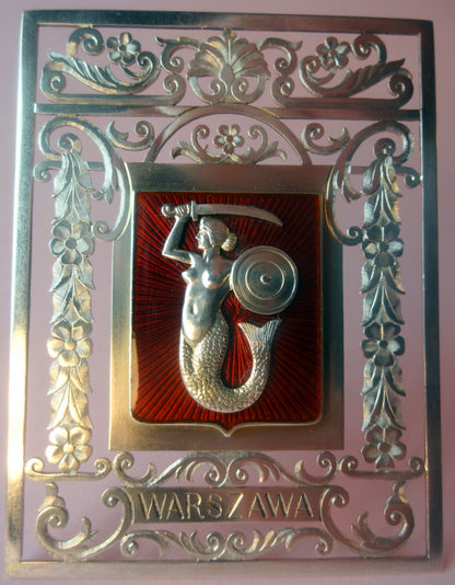Udskåret kraftig sølvplade, udskåret og mejslet, med loddet motiv af Warszawa byvåben, lavet af sølv og gennemskinnelig emalje. På forsiden graveret Waraszava, på bagsiden bordstøtte og indgraveret tekst.